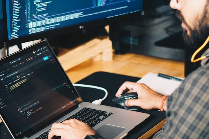 Mann am Laptop bei der Arbeit - Unsplash Bild Ein Mensch arbeitet an einem Laptop mit offenem Code und nutzt eine Maus.